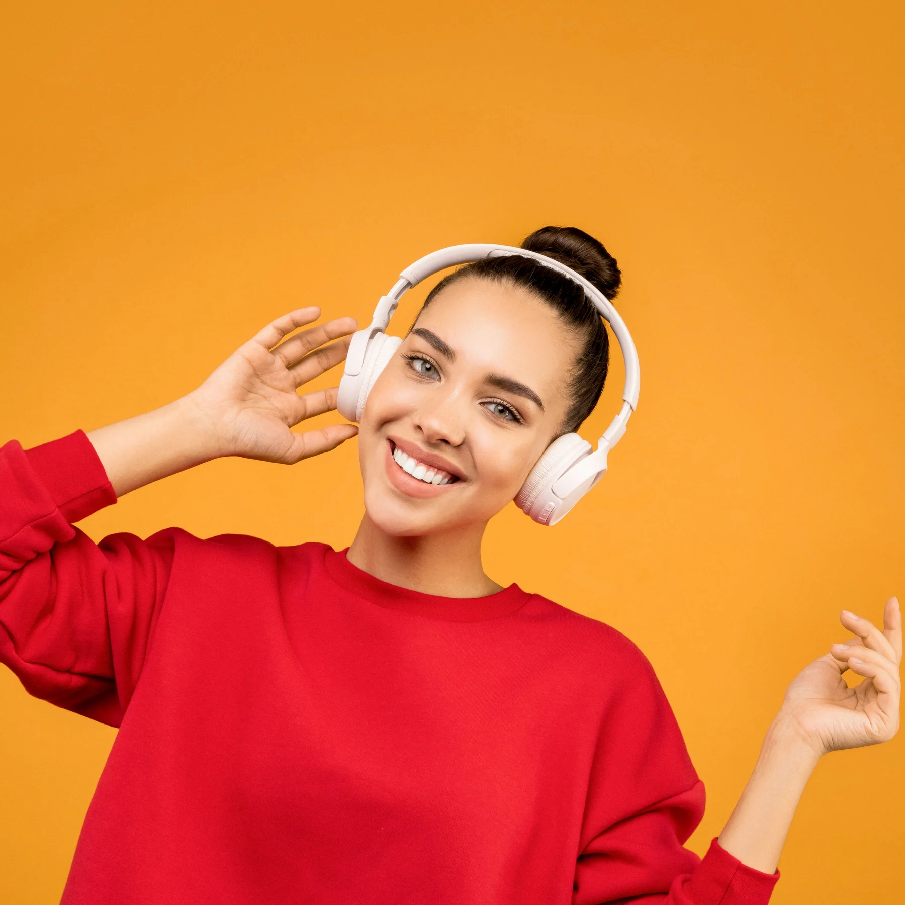 Pessoa sorrindo com fones de ouvido brancos e blusa vermelha, diante do fundo amarelo da marca.