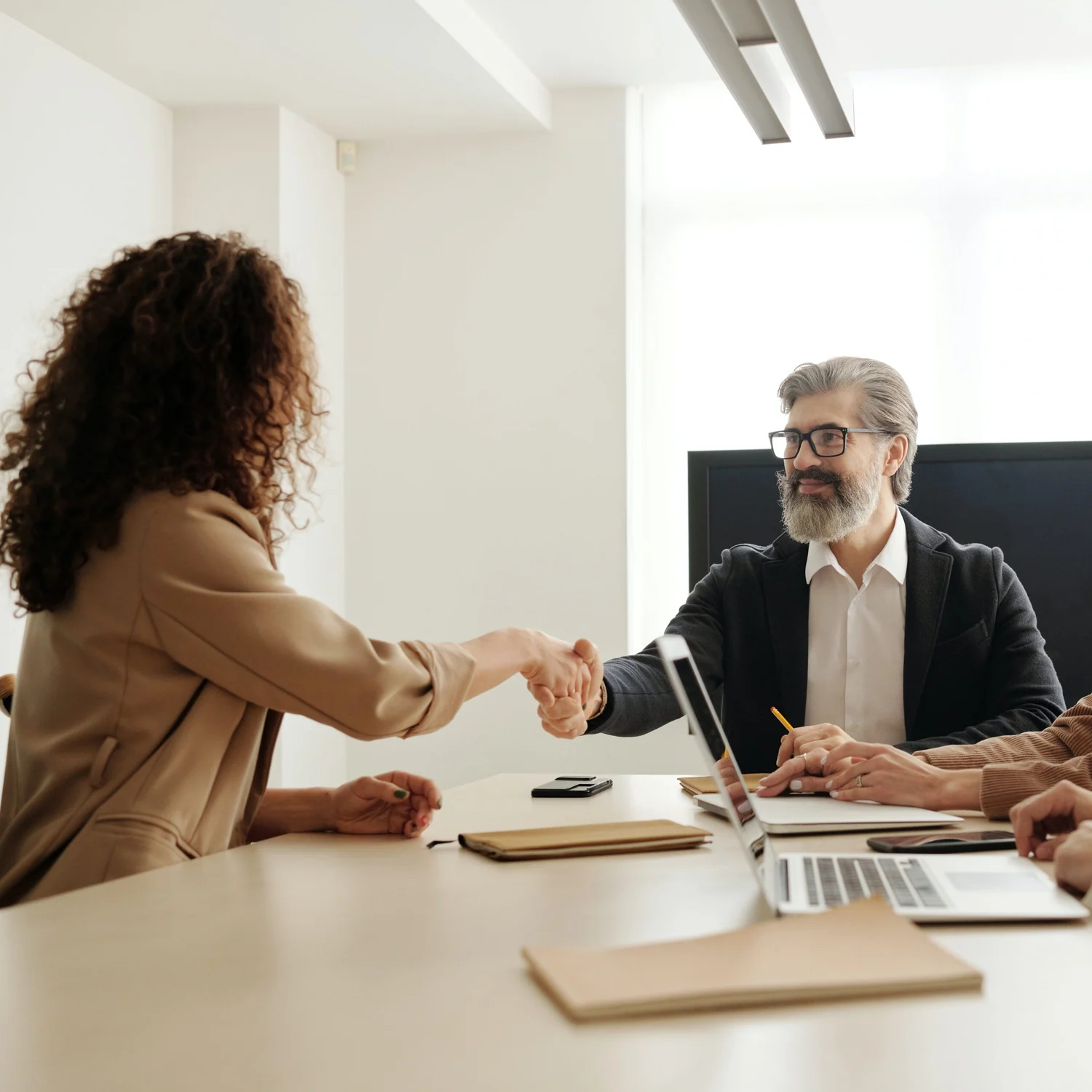 Parceiros selando uma parceria comercial com um aperto de mãos em sala de reunião moderna.